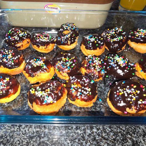 Freshly baked chocolate-glazed doughnuts topped with colourful sprinkles in a glass dish