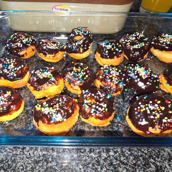 Freshly baked chocolate-glazed doughnuts topped with colourful sprinkles in a glass dish